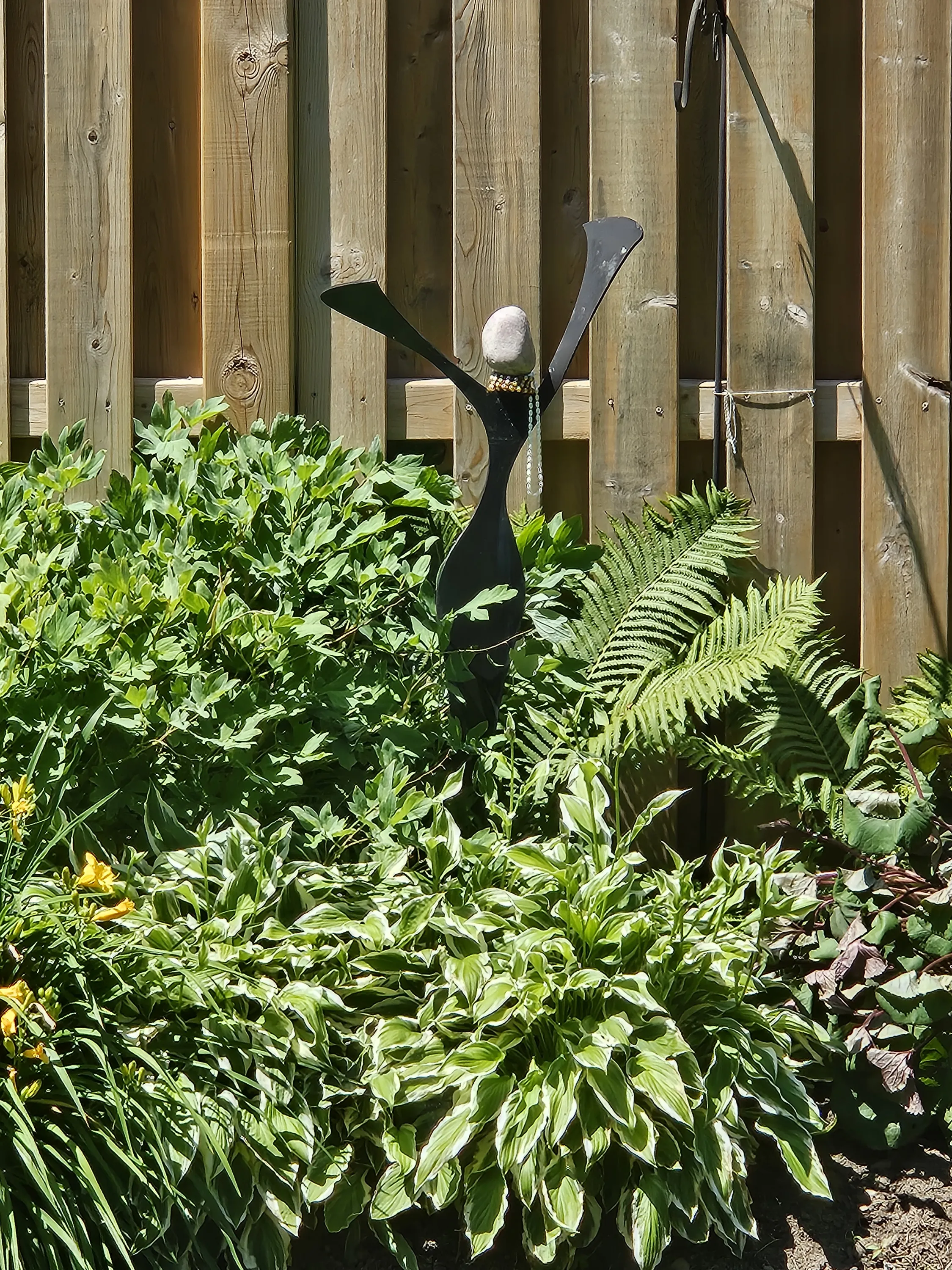 Garden sculpture with a stone, arms raised among ferns and hostas